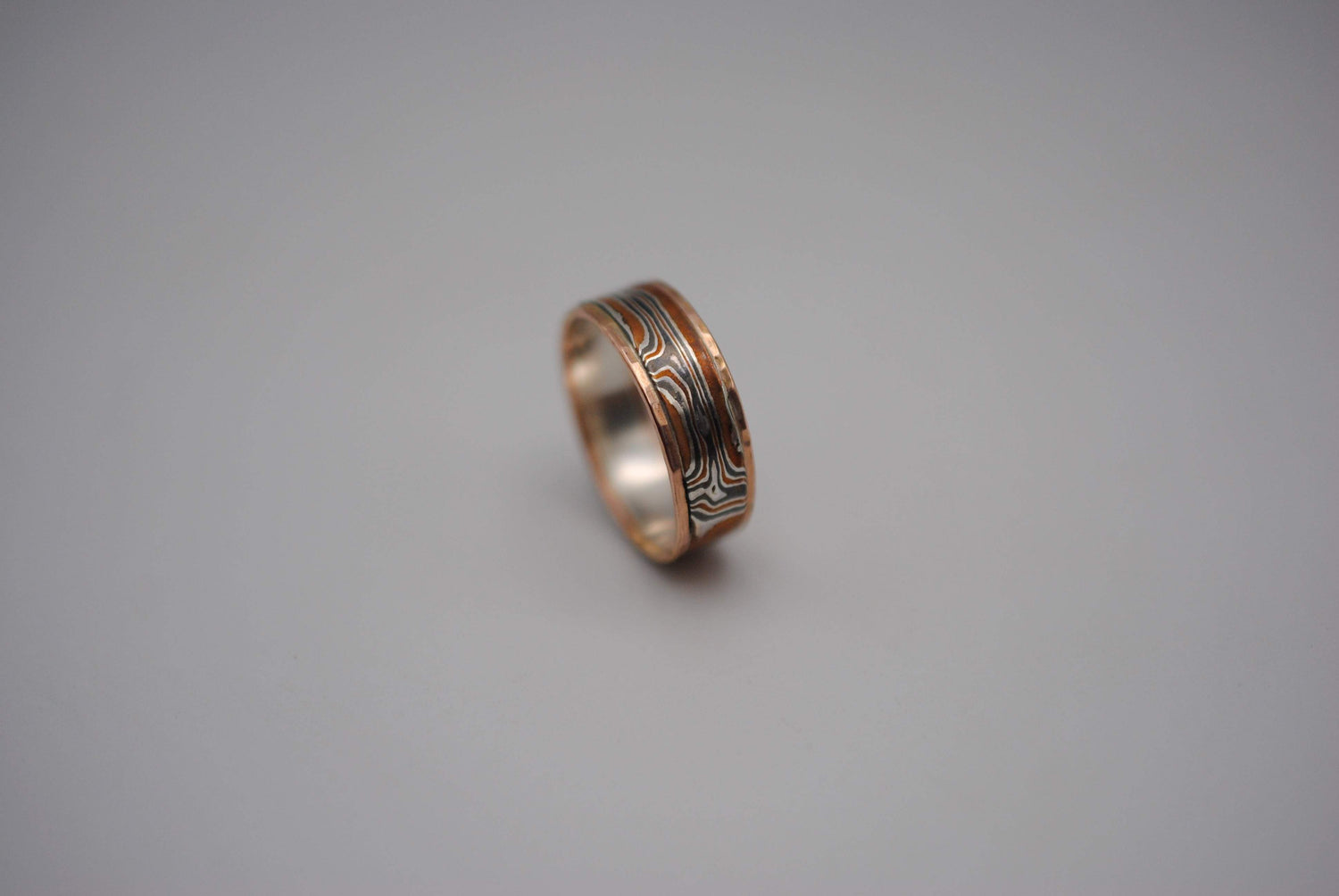 A mokume gane ring band. Mokume gane means metals that look like woodgrain. It's banded in Rose Gold. This frames in the woodgrain.