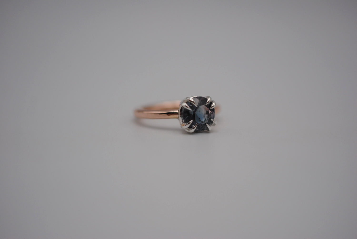 A blue tourmaline ring with double silver prongs on a rose gold band.