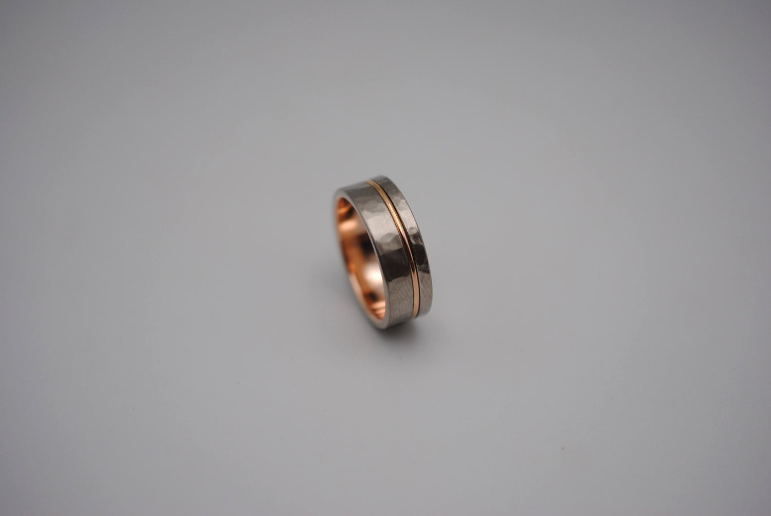 A men's styled wedding ring band. It's Palladium White Gold (a beautiful grey color) with a Rose Gold Inlay. It is hammred textured and brushed finished.