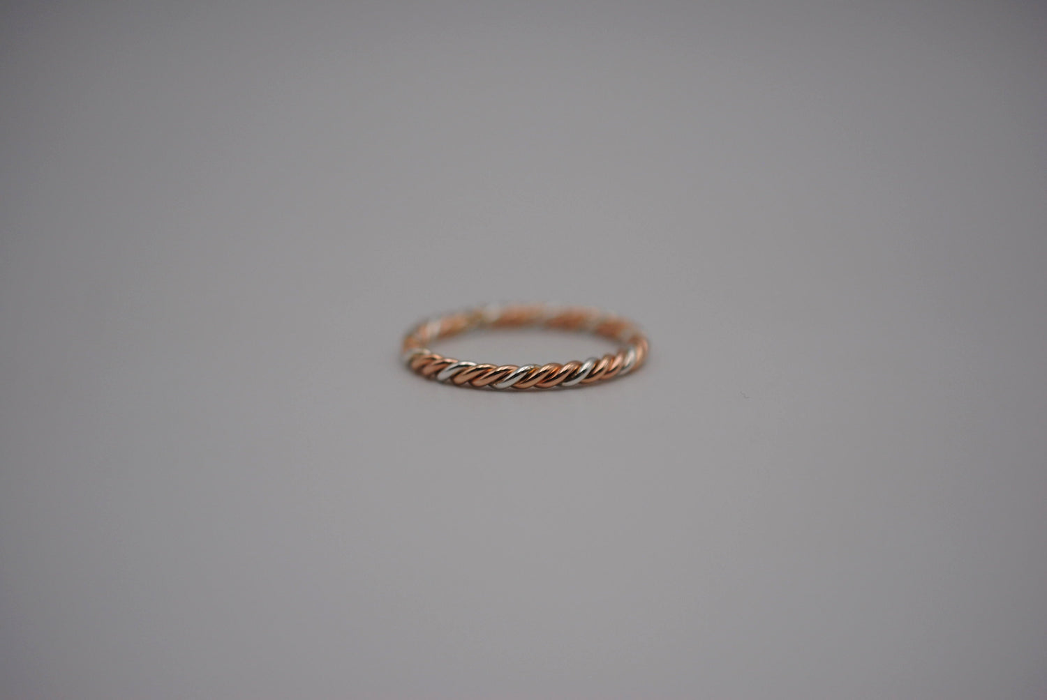 A mixed metal rope ring with yellow gold, rose gold, and silver weaved together.